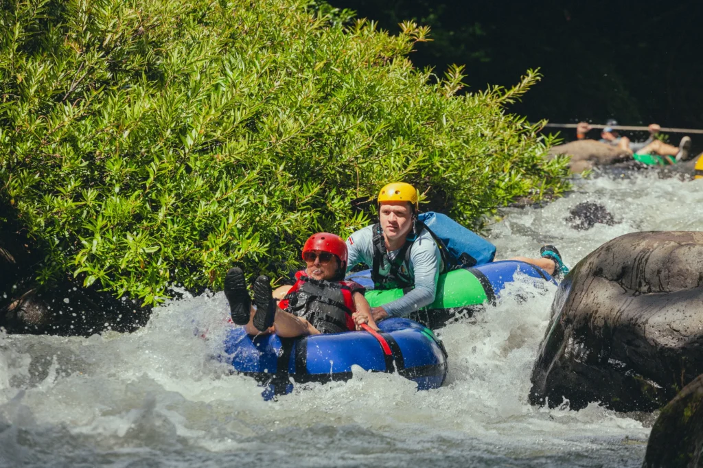 Participants wearing helmets and life jackets tubing through rapids in Curubandé, Liberia